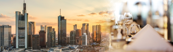 Die Frankfurter Skyline bei Sonnenuntergang fließt in das Bild eines elegant gedeckten Tisches ein.