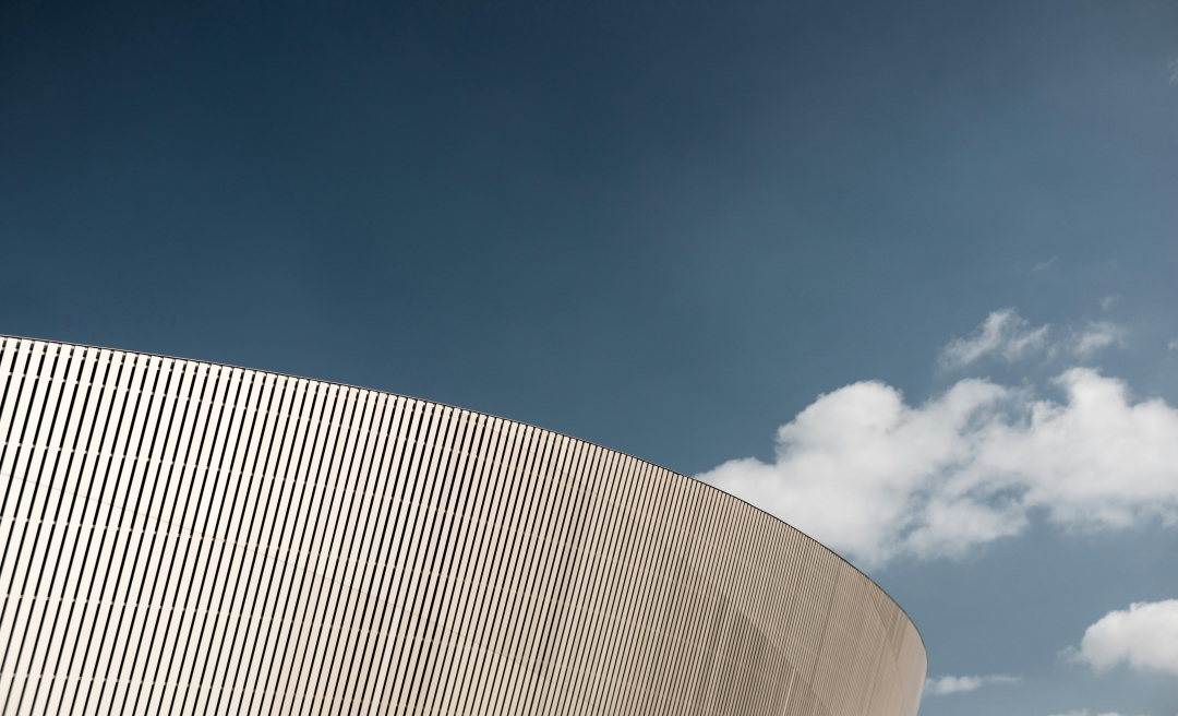 Foto: Eine futuristische, runde Fassade vor blauem Himmel mit weißen Wolken.