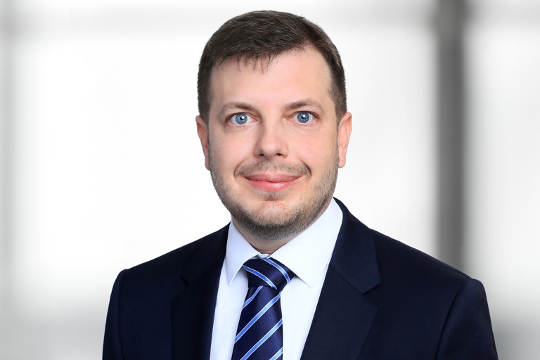 Foto: Porträt von Florian Bandrack. Er trägt einen dunkelblauen Anzug und eine dunkelblau-gestreifte Krawatte.
