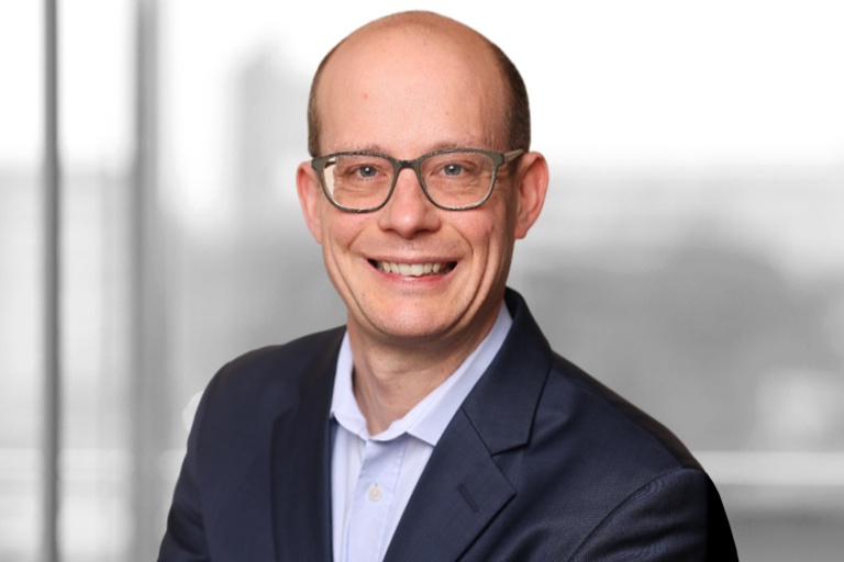 Foto: Andreas Roehr lächelt freundlich in die Kamera. Er trägt einen dunkelblauen Anzug und eine weißes Hemd.