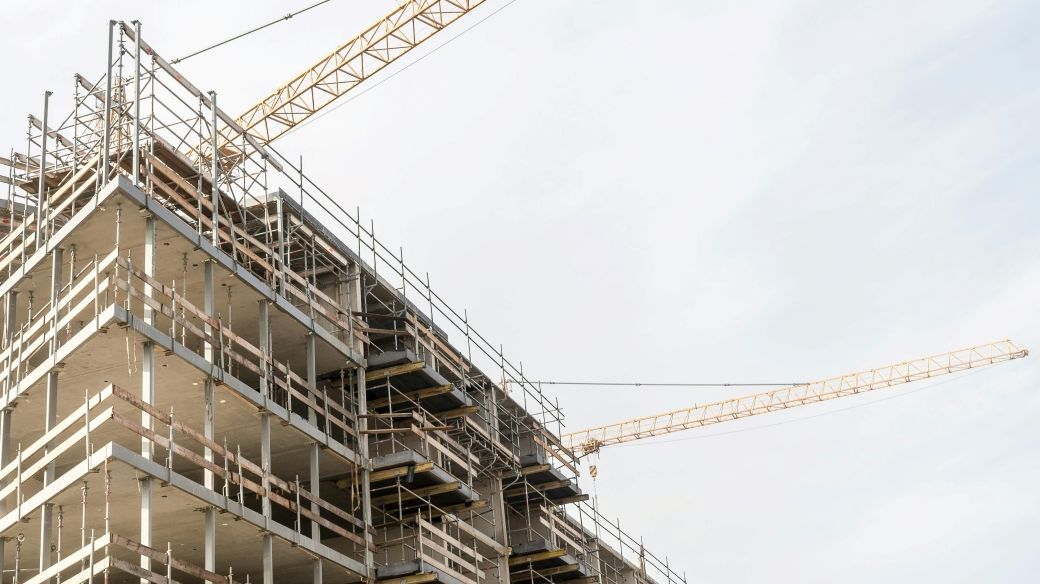 Foto: Ein Rohbau eines großen Mehrparteiengebäudes mit Gerüst und Kränen.