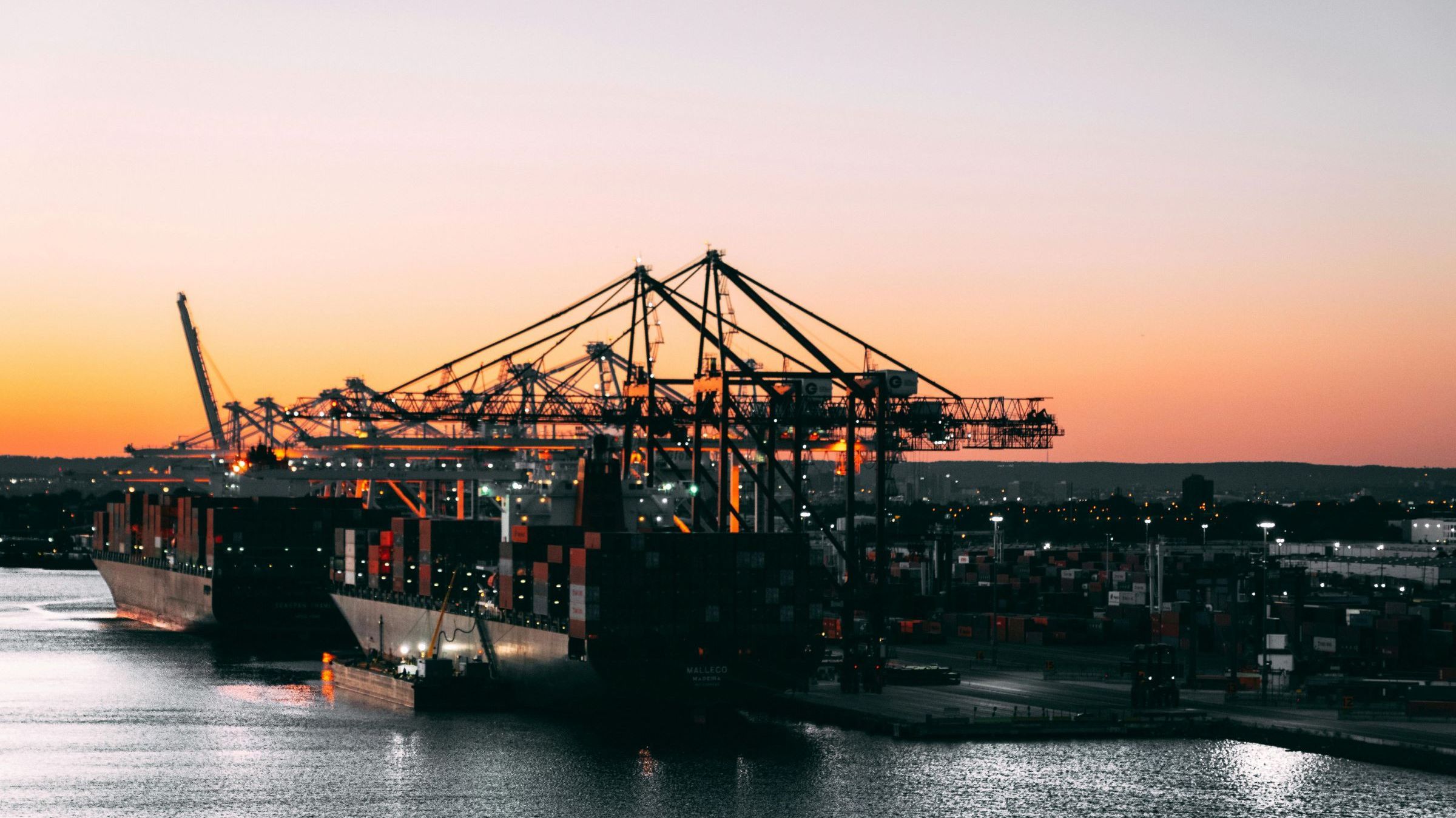 Bild: Containerhafen bei Sonnenuntergang, mit großen Frachtschiffen und zahlreichen Kränen