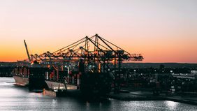 Bild: Containerhafen bei Sonnenuntergang, mit großen Frachtschiffen und zahlreichen Kränen