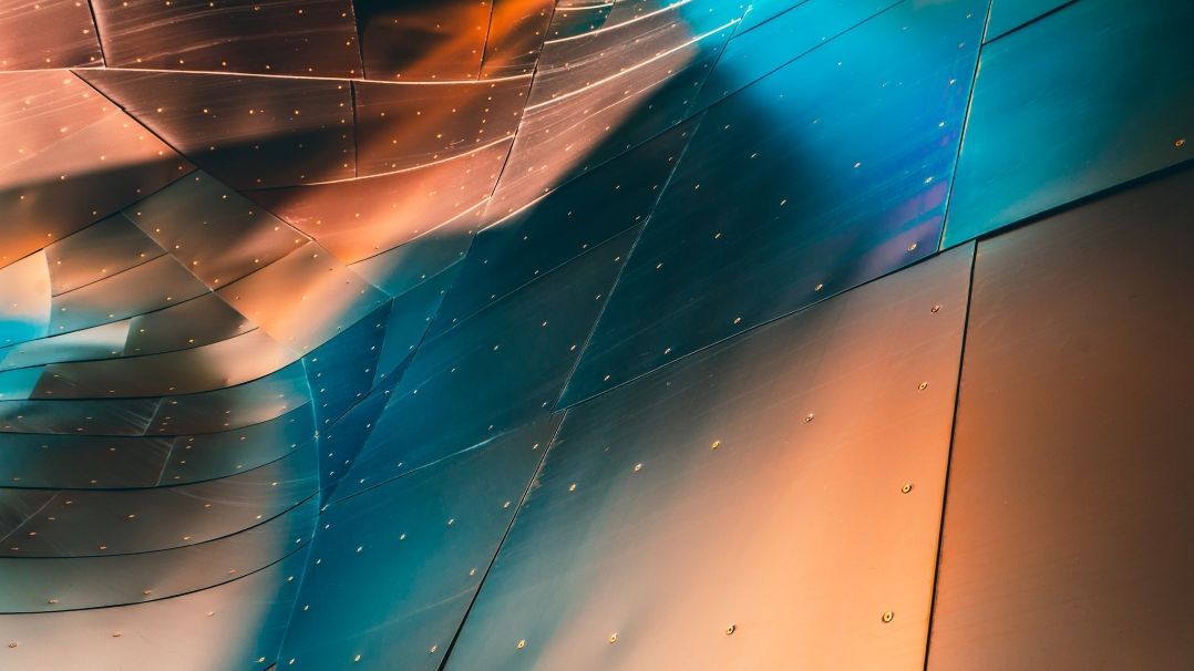Geschwungene, aneinander genietete Metallplatten werden orange und blau angestrahlt.