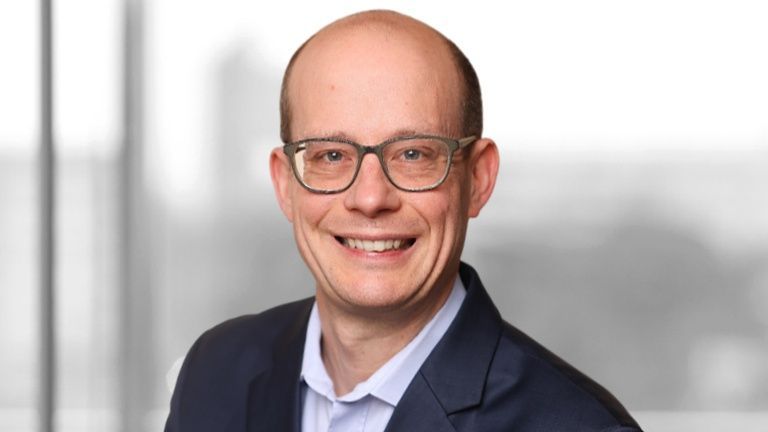 Foto: Andreas Roehr lächelt freundlich in die Kamera. Er trägt einen dunkelblauen Anzug und eine weißes Hemd.