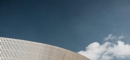 Foto: Eine futuristische, runde Fassade vor blauem Himmel mit weißen Wolken.