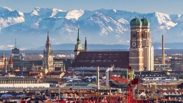 Blick auf die Frauenkirche in München mit den Alpen im Hintergrund