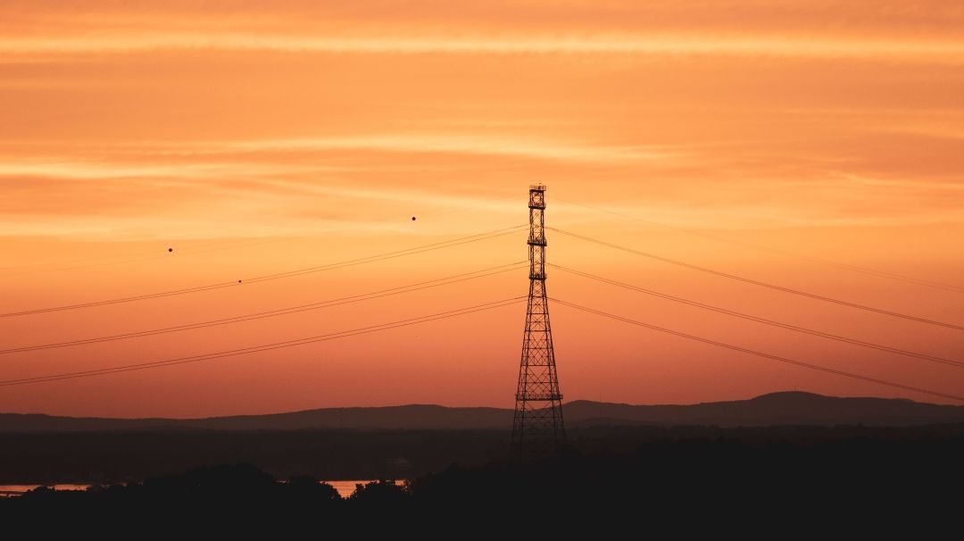 Ein Strommast steht im organge-roten Sonnenuntergang.