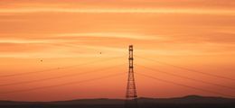 Ein Strommast steht im organge-roten Sonnenuntergang.