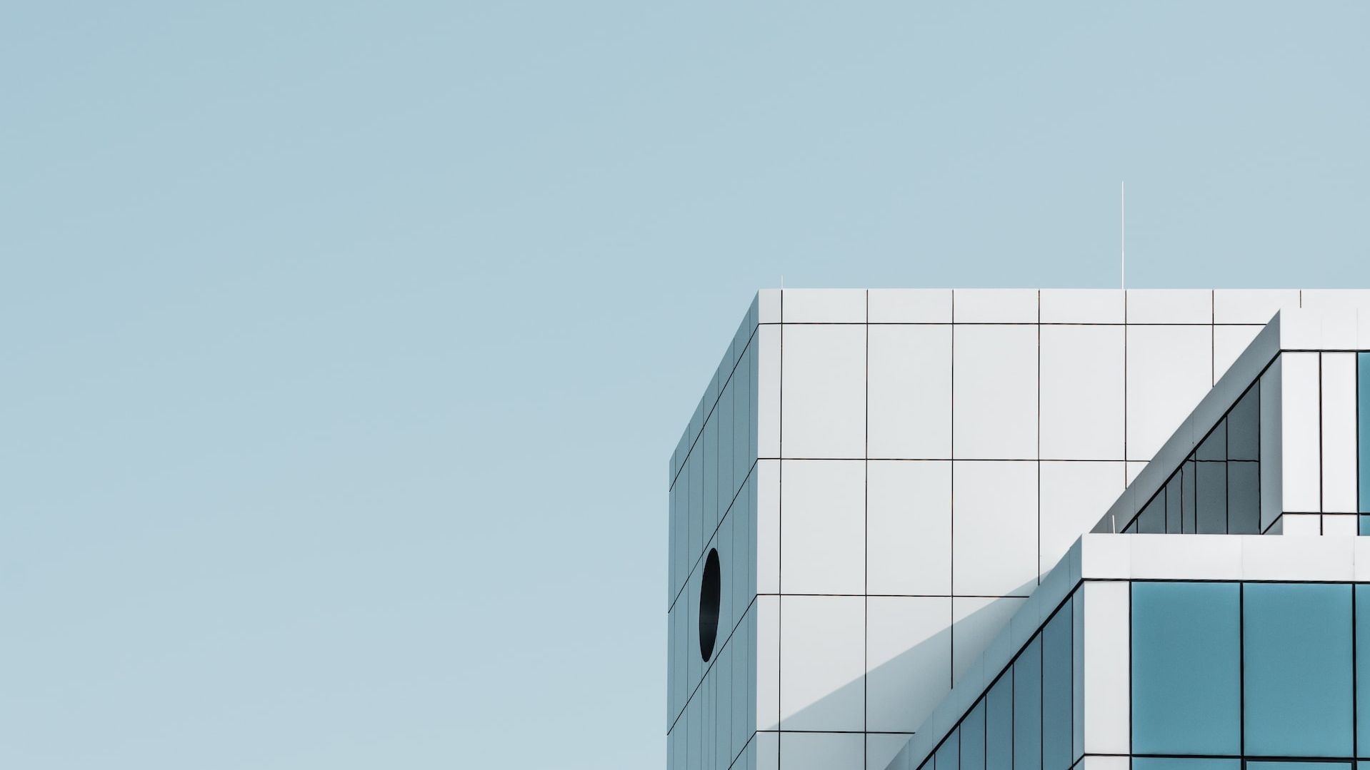 Foto: Ein Bürogebäude mit sehr eckigen Formen vor hellblauem Himmel. Es hat weiße und gläserne Fassagenteile.