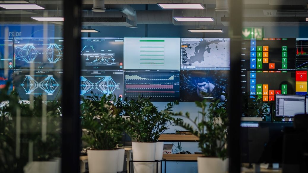Image: a modern control center with multiple screens displaying various data visualizations, maps and analyses