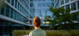 Eine Frau steht vor einem Bürogebäude. Die hält Vertragsunterlagen in der Hand.