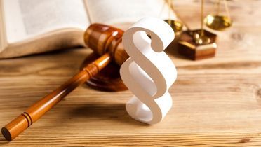 weißes Paragraphsymbol mittig auf einem Tisch neben einem Richter Gavel