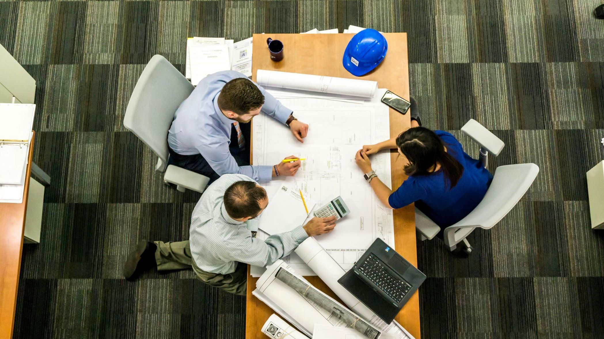 Picture: three people looking at a floor plan drawing on the table.
