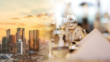 Die Frankfurter Skyline bei Sonnenuntergang fließt in das Bild eines elegant gedeckten Tisches ein.
