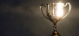 Foto: Ein goldener, glänzender Pokal steht vor einer dunklen Wand.