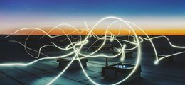 Foto: Fach im Morgengrauen. Durch Neonlichter werden Stromleitungen angedeutet.