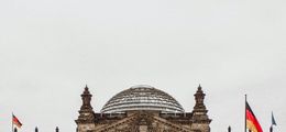 Foto: Das Reichstagsgebäude in Berlin, vor grauem Himmel, von vorn fotografiert.