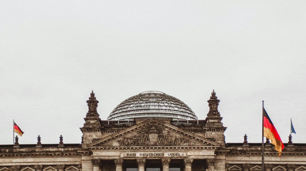 Foto: Das Reichstagsgebäude in Berlin, vor grauem Himmel, von vorn fotografiert.