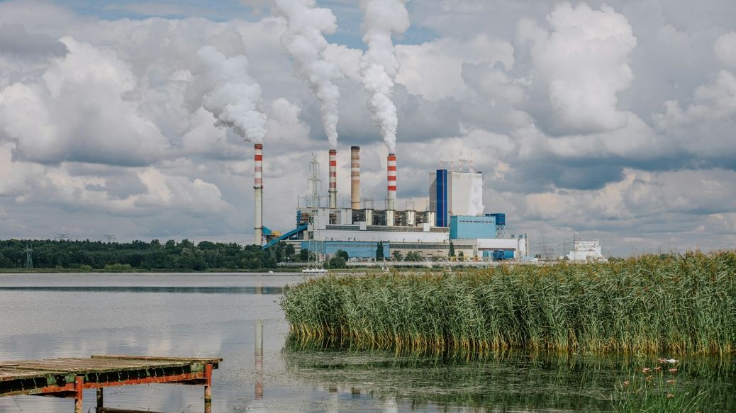 Picture: a large factory with smoking chimneys on the shore of a lake.