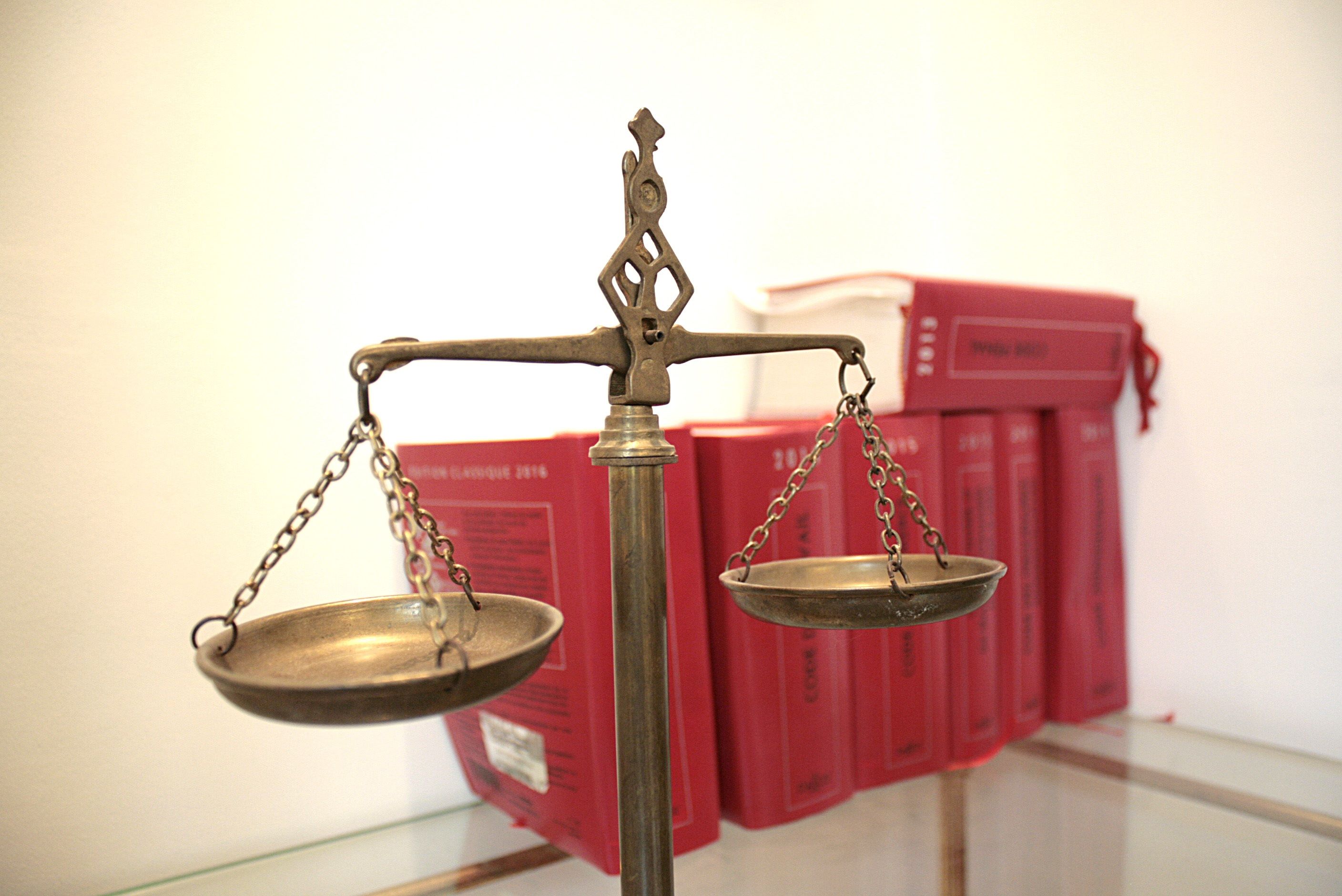 Photo: a classic metal beam scale standing on a glass surface with red law books in the background